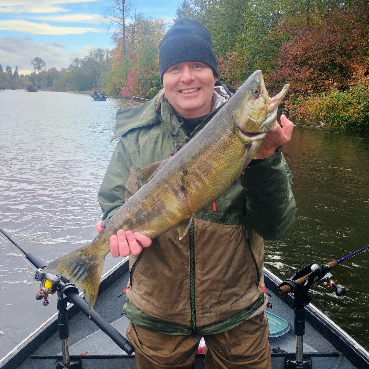 Person holding a large fish on a boat with water and trees in the background